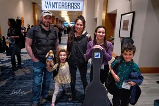 A family with instrument cases posing at the Wintergrass festival backdrop