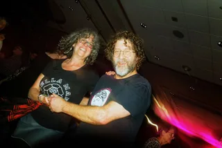 Two smiling festival-goers arm in arm on the dance floor under pink stage light at Wintergrass
