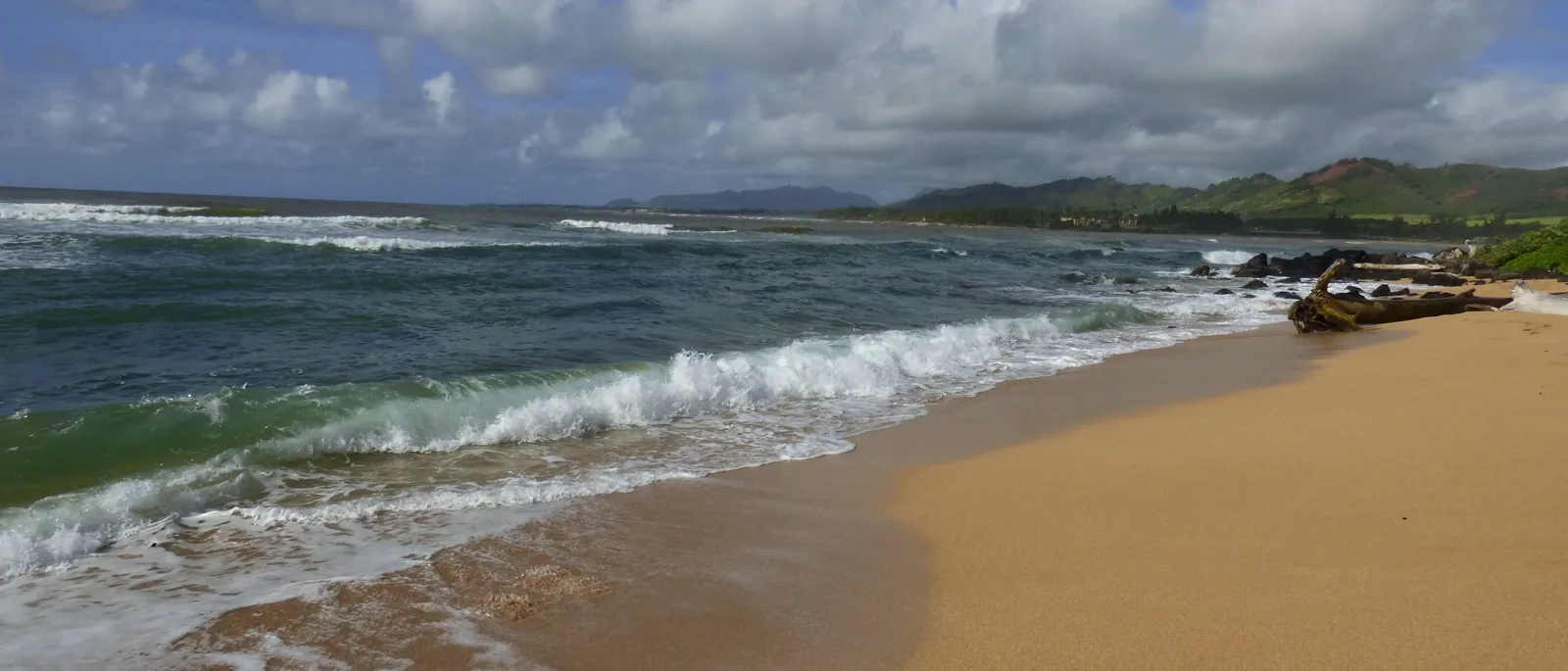Waves rolling onto the sand with Kauai's green hills in the distance