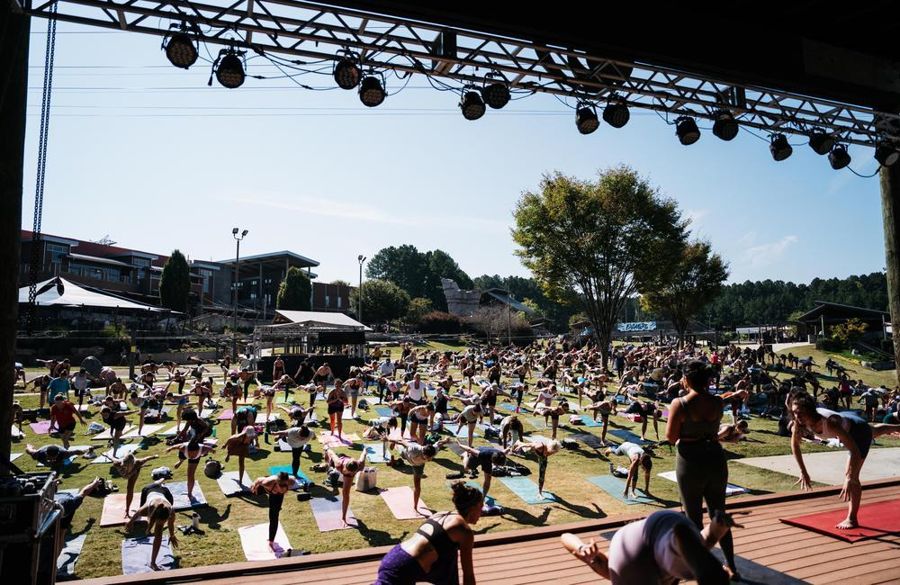 Hundreds of practitioners mid-flow on mats across the Whitewater Center lawn at Flow Fest, seen from the main stage