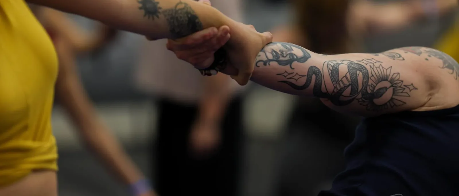 Two tattooed arms clasp in a partner stretch at Grand Valley Yoga Fest