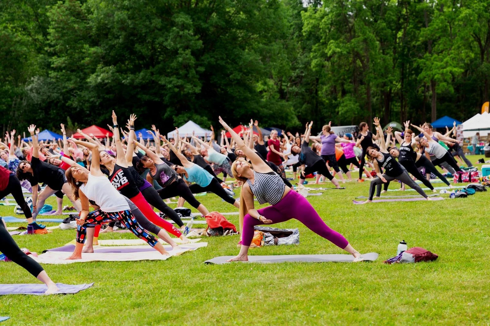 Outdoor festival class in side-angle pose across a tented lawn
