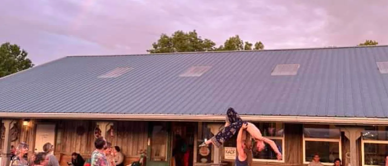A rainbow arcs over the festival lodge as an acro-yoga pose is lifted at Kentucky Yoga Festival