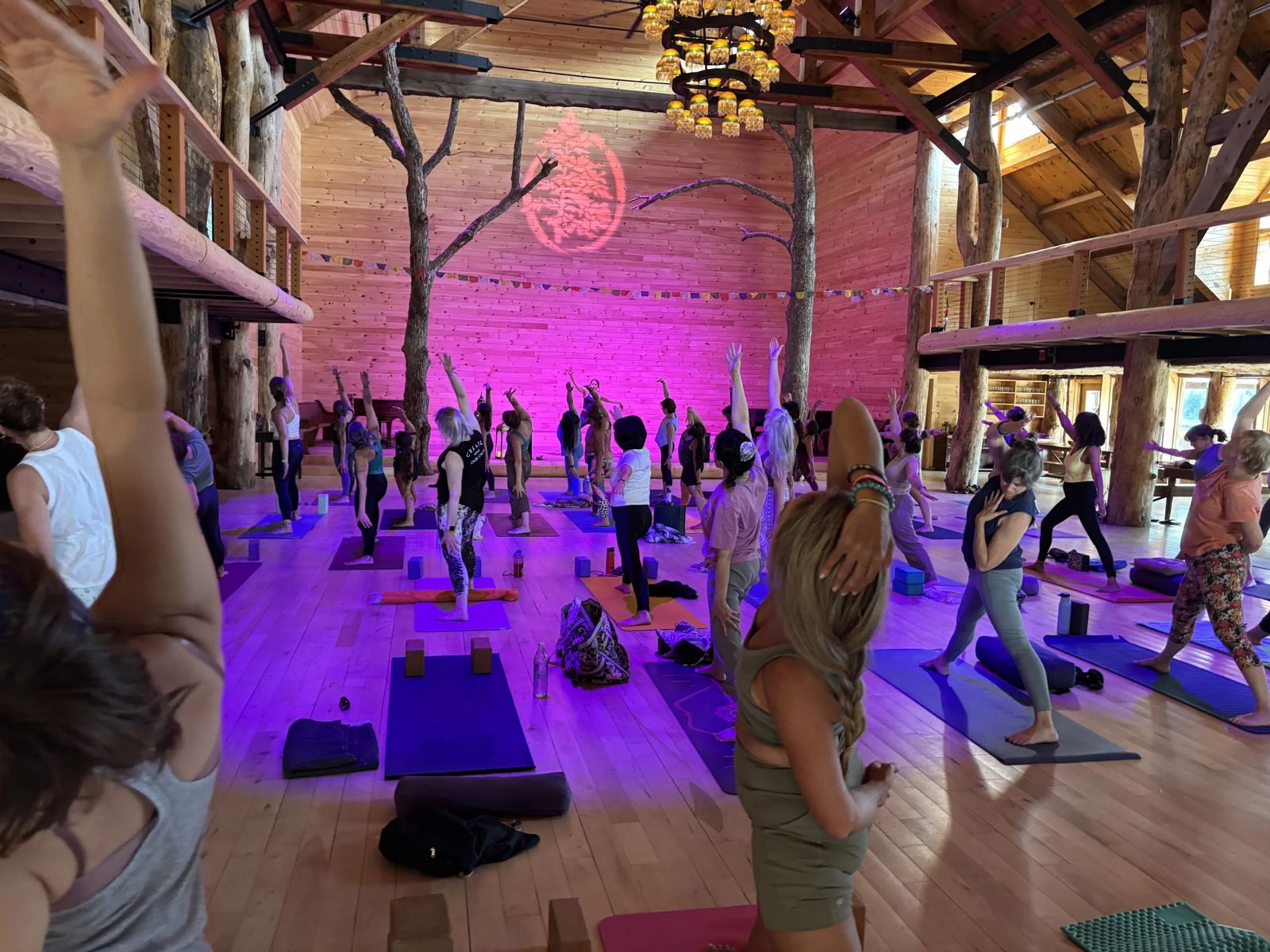 Warrior pose class beneath the timber beams and glowing chandelier of the Ogontz lodge at Kula Yoga Fest