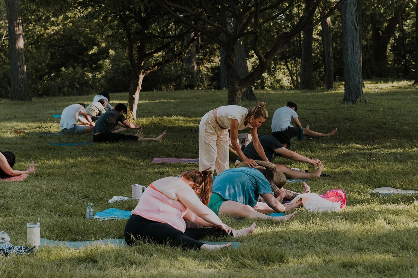 An instructor guides seated stretches under park trees at Mandala Yoga Festival