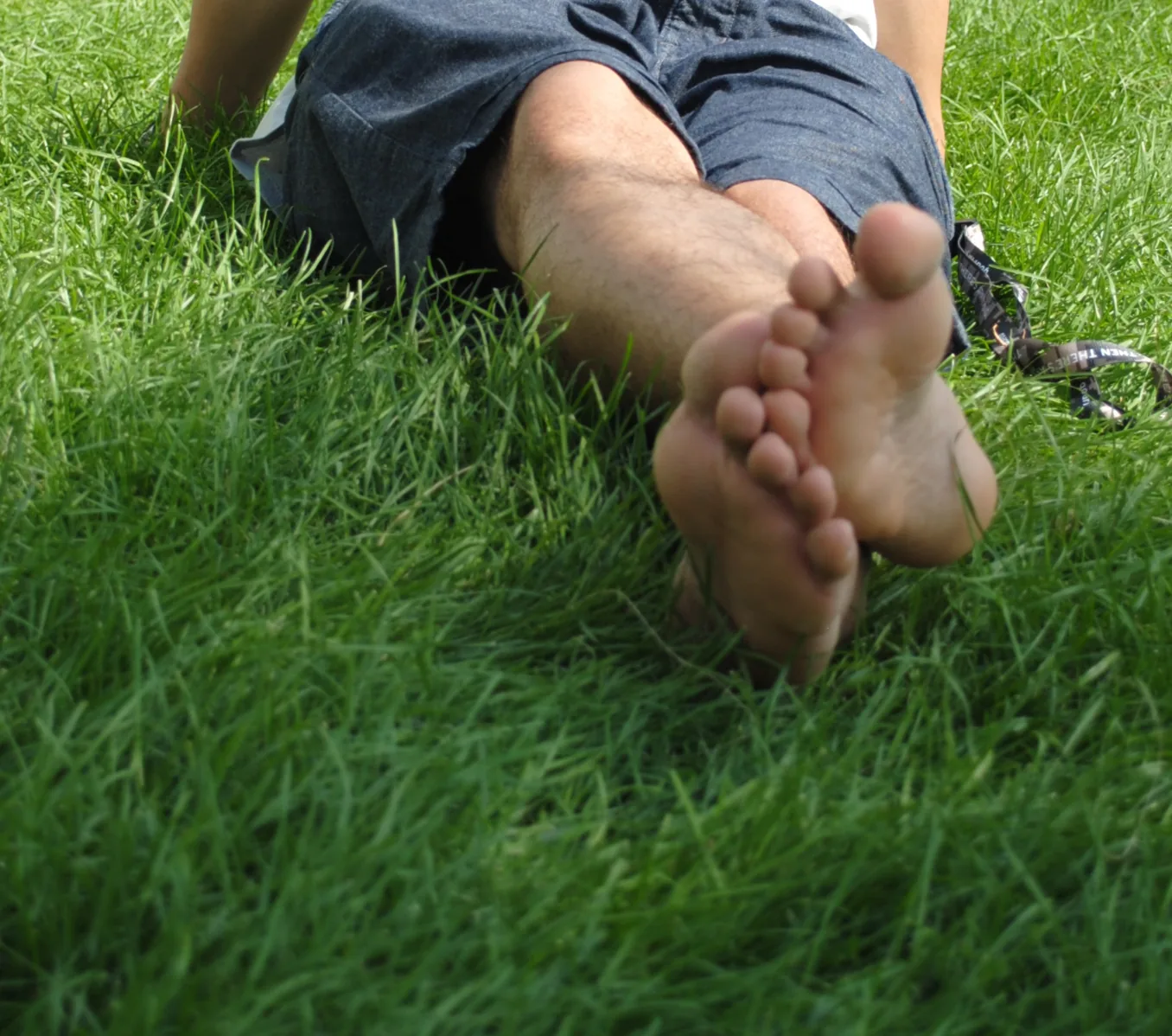 The bare feet and lower legs of a person lying on a lawn, soles toward the camera, with grass filling the frame.