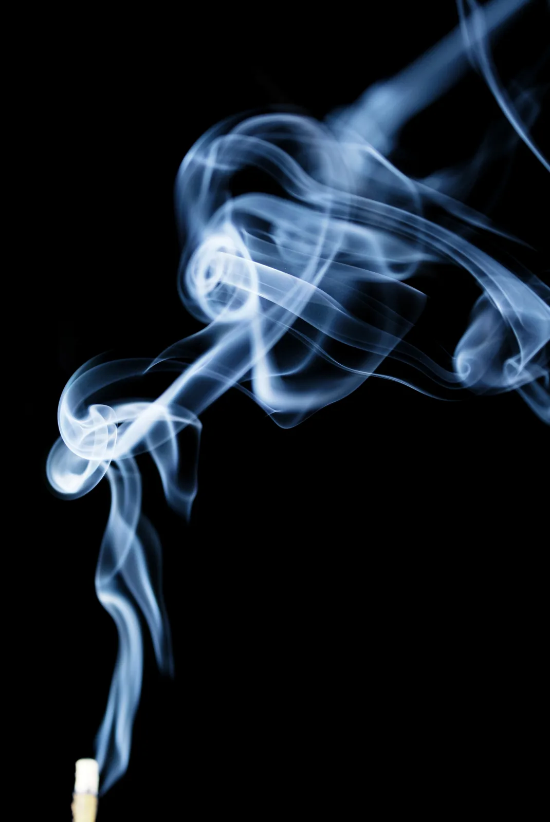 A single incense stick burning, its thin smoke curling upward against a dark background.