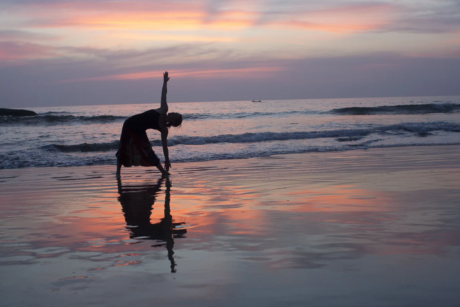 A person bending backwards on a wet beach at dusk, reflected in the shallow water, with pink cloud along the horizon.